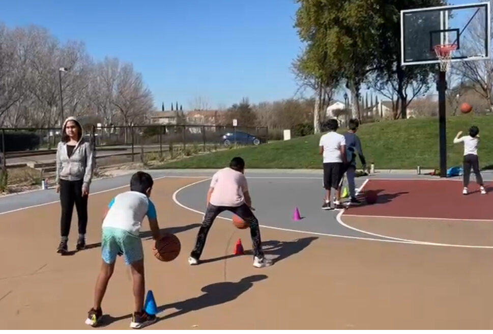 Kids practicing a dribbling drill through cones on an outdoor court