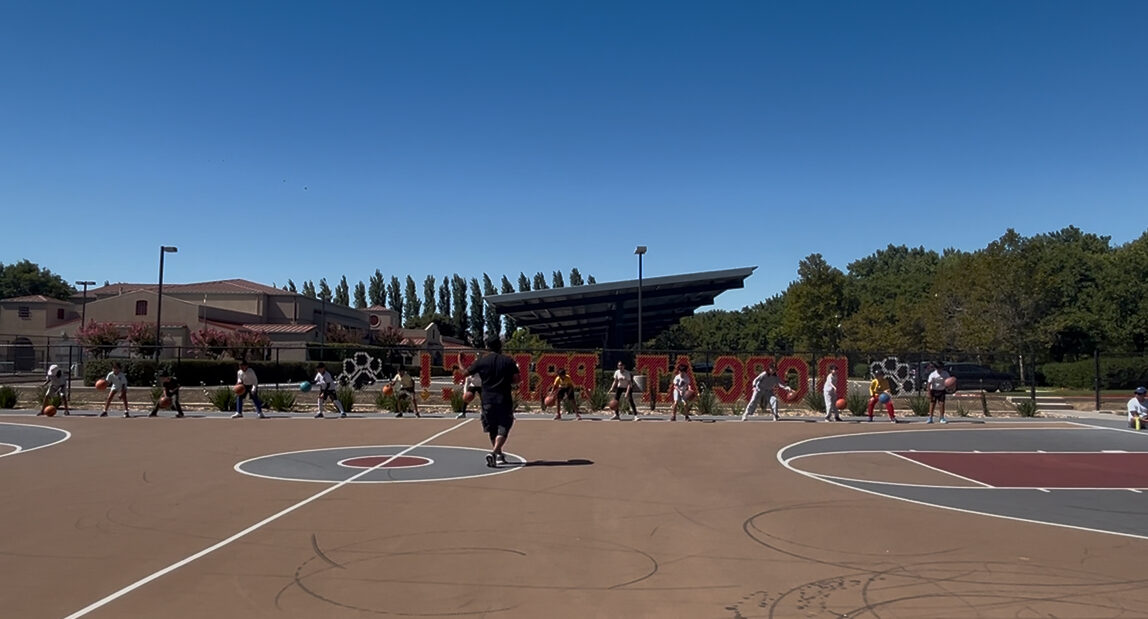 Youth players running a dribbling drill line on an outdoor basketball court